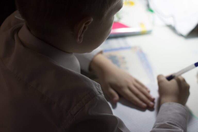 Niño pequeño escribiendo en un cuaderno, con lápiz en mano, en un aula escolar.